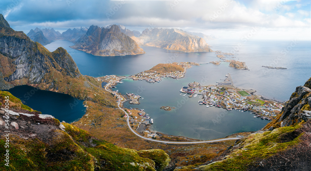 Panorama view during sunset or sunrise from the top of Reinebringen, Norway. View from mountain on fjords and Reine fishing village in Lofoten island. Steep mountains.