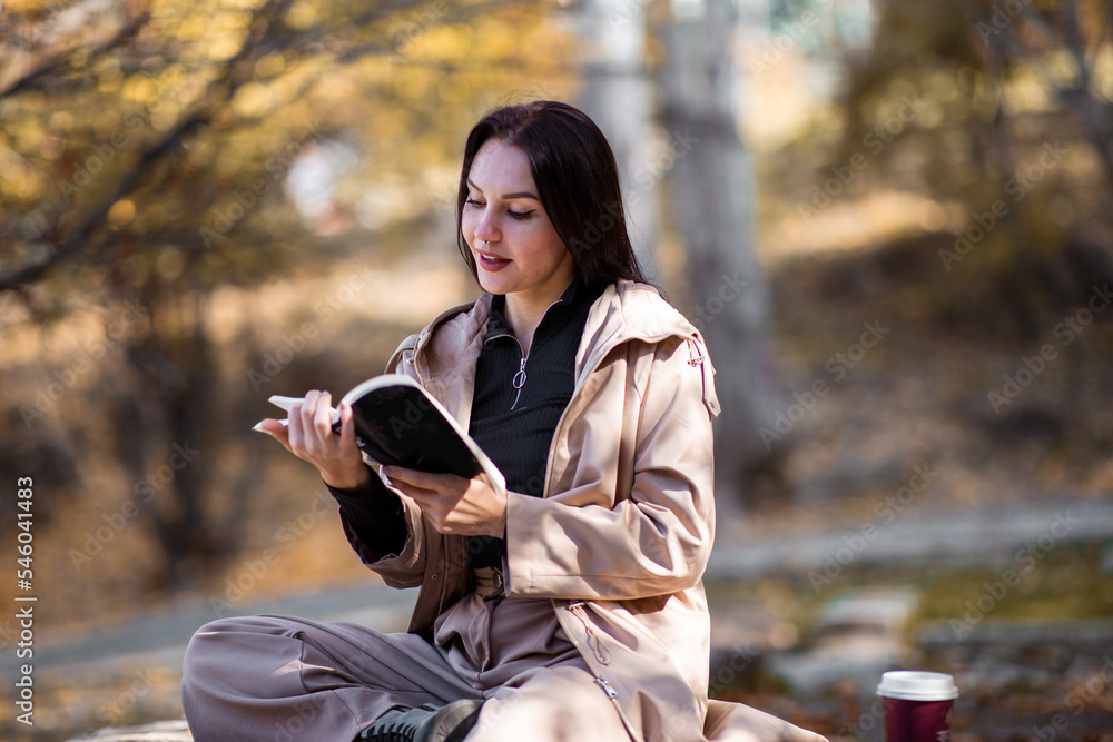Happy stylish woman portrait in autumn season with trenchcoat she is drinking coffee and reading book. Happy stylish woman portrait in autumn season with trenchcoat she is drinking coffee and reading book.