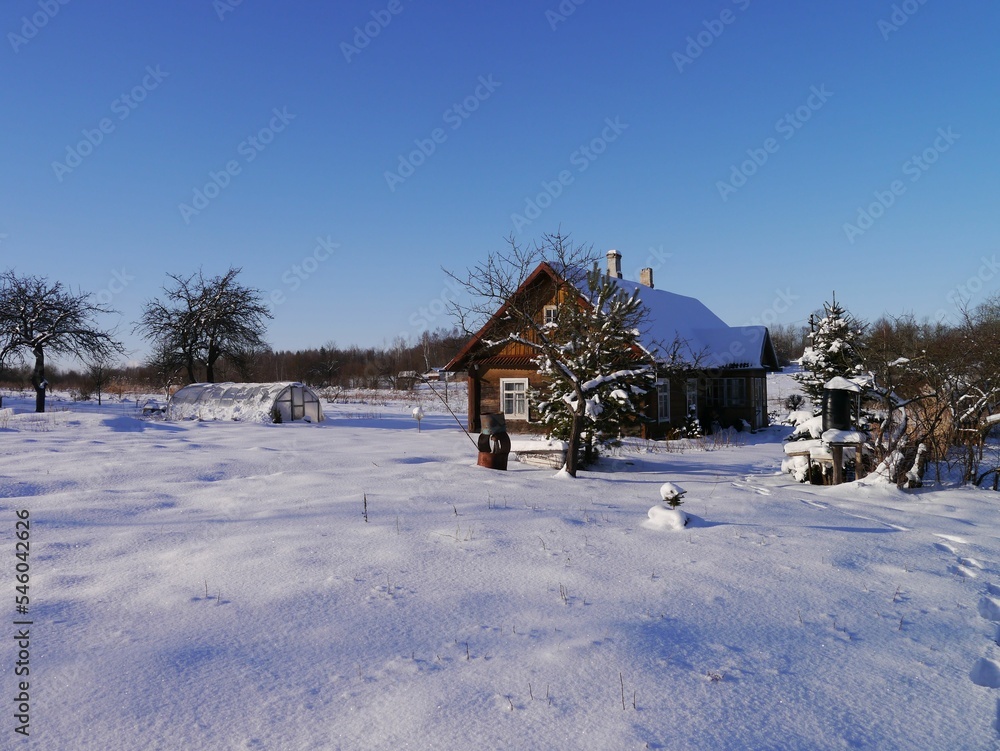Scenic shot of a snow-covered field with a wooden house on a sunny day Scenic shot of a snow-covered field with a wooden house on a sunny day