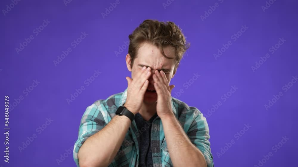 Tired fatigued young man 20s with migraine headache posing isolated on purple background studio. People lifestyle concept. Put hands on head temples Tired fatigued young man 20s with migraine headache posing isolated on purple background studio. People lifestyle concept. Put hands on head temples