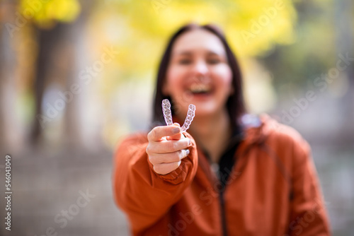 Happy young woman smiling with invisible teeth aligner during fall season at park.