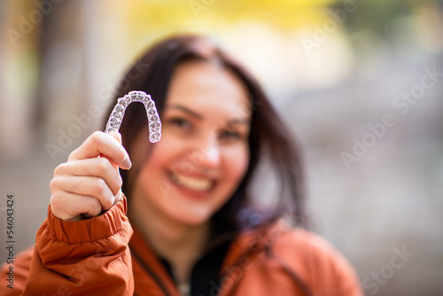 Happy young woman smiling with invisible teeth aligner during fall season at park.