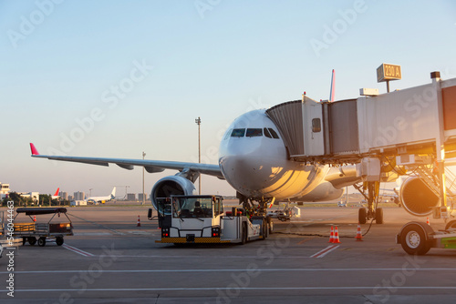 Aircraft is attached to the terminal gangway of the airport building preparation for towing and launch flight in the evening at sunset.