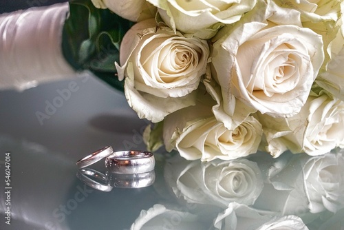 Closeup shot of wedding rings against the bouquet of white roses