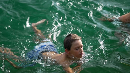 Preteen kid swimming in lake. Child swimmer in great outdoors in slow motion. Active young boy swims outside. Candid and authentic