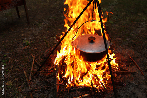 Cooking outdoors in field conditions. Cauldron on a fire in the forest. Cooking at the stake while traveling. Tripod with a bowler hat on a fire on picnic. Conceptual travel, trekking and adventure