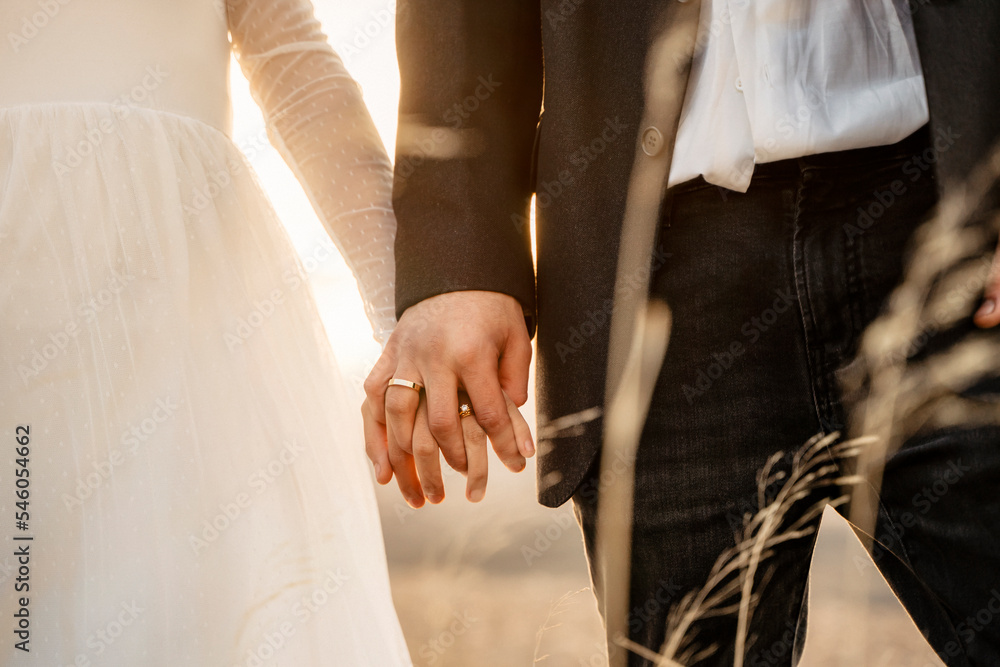 Φωτογραφία Pareja de recién casados dandose la mano en puesta de sol y mostrando las alianz