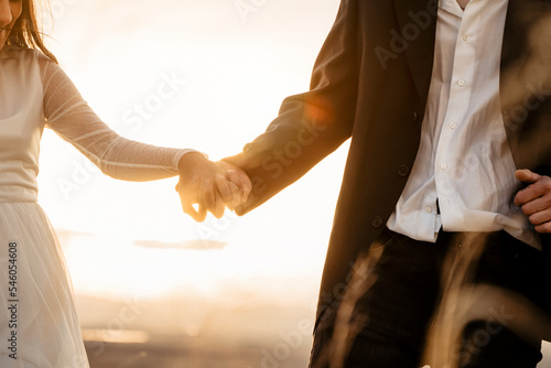 Pareja de recién casados dandose la mano en puesta de sol y mostrando las alianzas photo