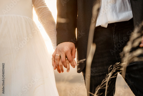 Pareja de recién casados dandose la mano en puesta de sol y mostrando las alianzas © Cristina