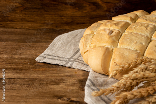 Close-up of ears of wheat and half a loaf of candeal bread on dark wooden table and background, selective focus, horizontal, with copy space