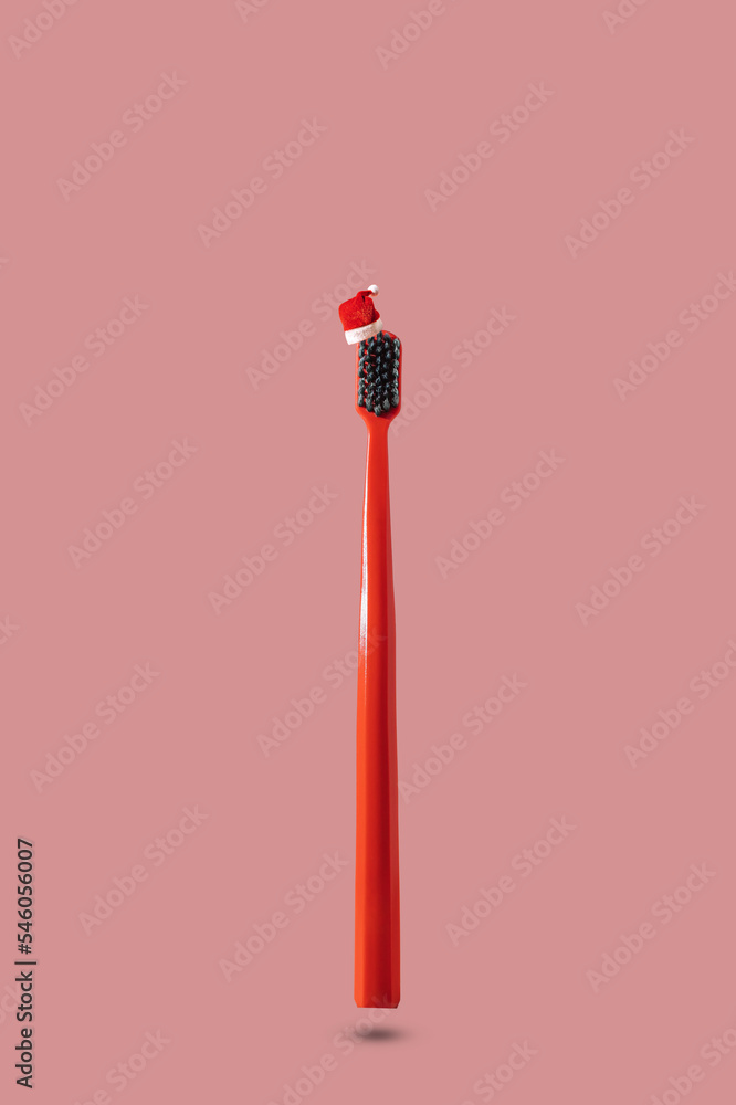 Single red toothbrush with red and white Santa hat floating on pink background with copy space. Dental medical Christmas and New Year concept. Creative medical health still life levitation. Single red toothbrush with red and white Santa hat floating on pink background with copy space. Dental medical Christmas and New Year concept. Creative medical health still life levitation.
