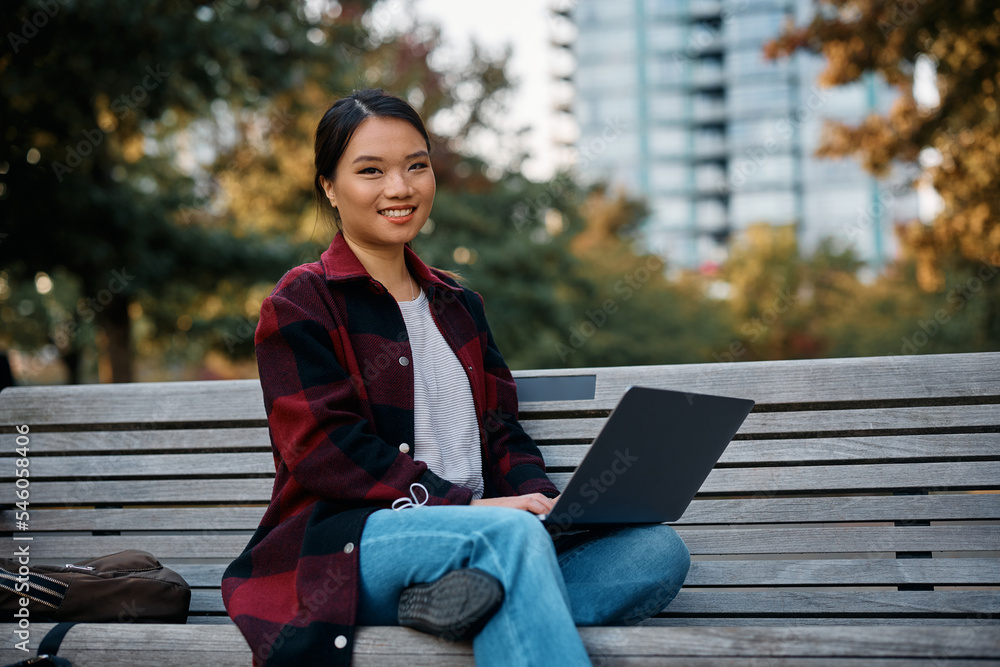 Happy Asian woman using laptop in park and looking at camera. Happy Asian woman using laptop in park and looking at camera.