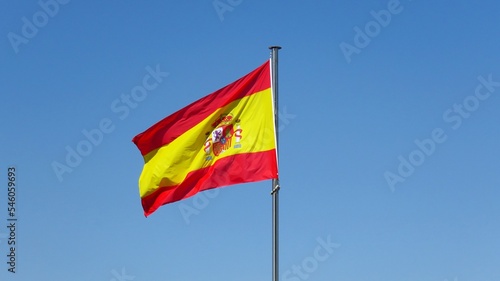National flag of Spain waving on the pole on the background of the blue sky