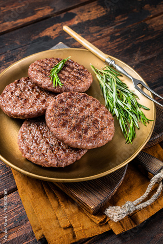 Grilled burger beef meat patty with herbs and spices on steel plate. Wooden background. Top view