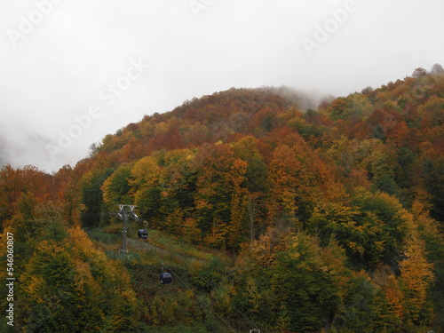 A modern cable car rides into the mountains, with cloudy sky in the background. Beautiful view of the cable car in autumn.