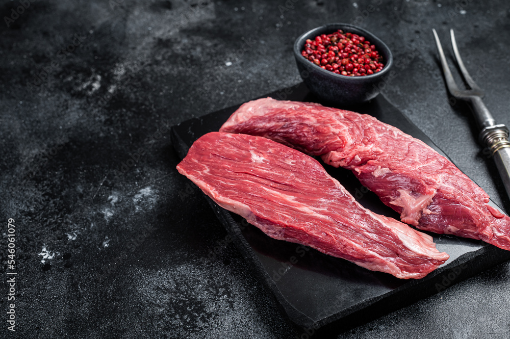 Bavette raw beef meat steak or Sirloin flap on marble board. Black background. Top view. Copy space