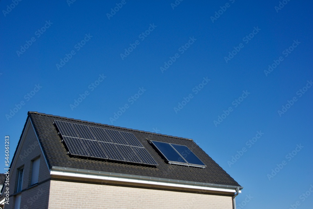 Fototapeta premium House with solar panels covering its tiled roof under a clear blue sky on a sunny day