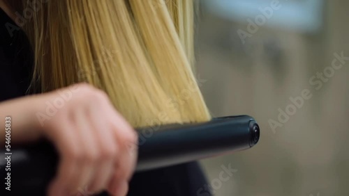 Young woman using a hair straightener in the bath in front of the mirror