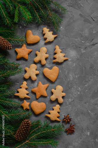 Christmas composition with homemade gingerbread cookies, fir tree branches, cones, star anise on a grey background. Copy space.