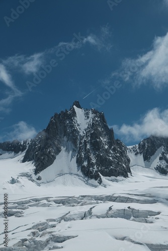 Vertical aerial view of rocky Alpine mountain peak with seracs in the foreground and blue cloudy sky