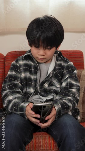 A young kid playing online game with his smartphone on the couch.