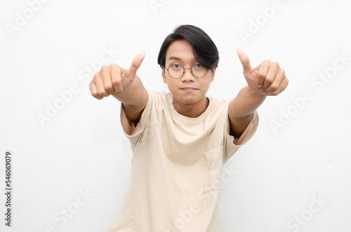 handsome attractive Asian man smiling happily and giving thumbs up as compliment isolated over white background. man giving approval and compliment by gesturing thumbs up.