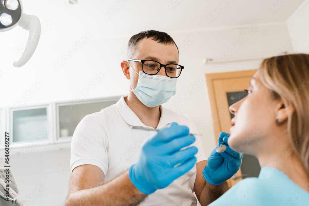 Fototapeta premium Consultation with dentist at dentistry. Teeth treatment. Dentist examines girl mouth and teeth and treats toothaches. Happy woman patient of dentistry.