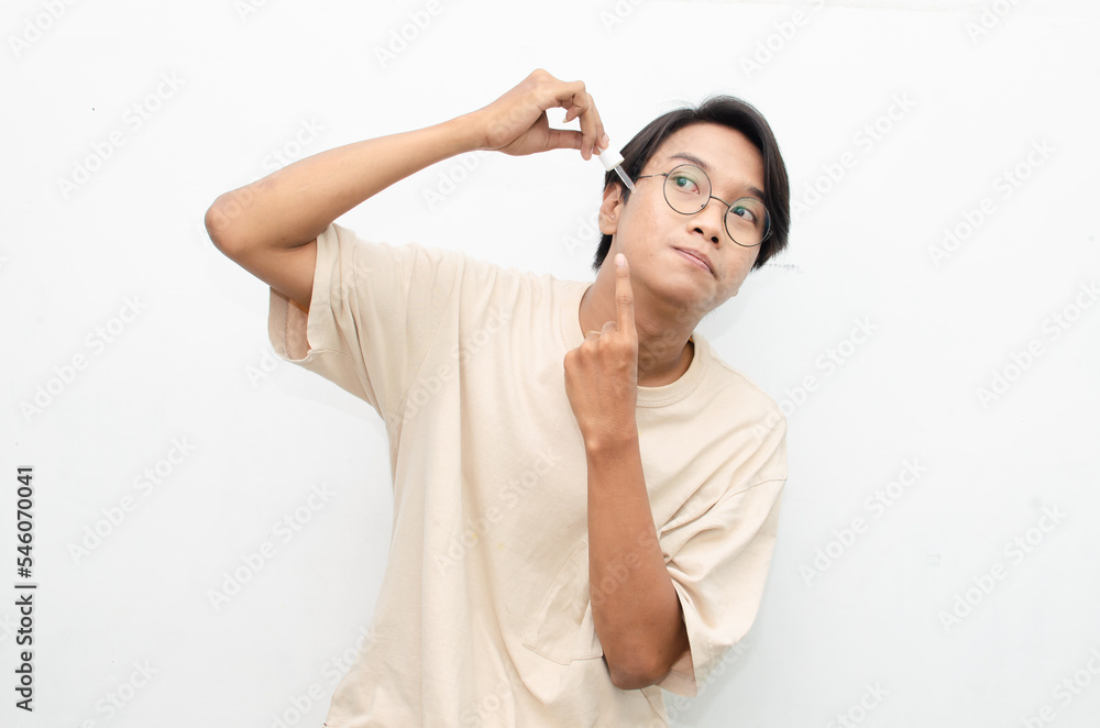 asian young man in casual beige tshirt applying beauty acne serum using pipette and smiling at camera isolated over red background asian young man in casual beige tshirt applying beauty acne serum using pipette and smiling at camera isolated over red background