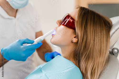 Dentist treats and removes caries in woman patient. Uv illumination of photopolymer tooth filling procedure at dentistry.