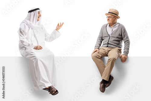 Arab man in a traditional robe sitting on a blank panel and talking to a senior man