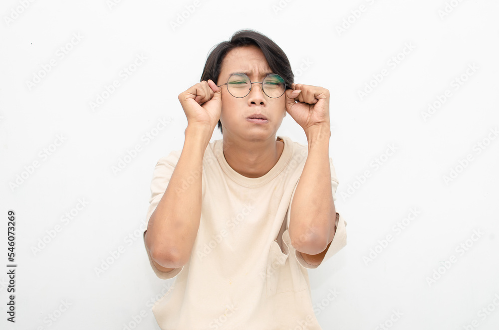 Young Asian man wearing glasses and beige tshirt with crying face expression isolated over white background. Crying face expression of Young Asian man with hand gesture. Young Asian man wearing glasses and beige tshirt with crying face expression isolated over white background. Crying face expression of Young Asian man with hand gesture.