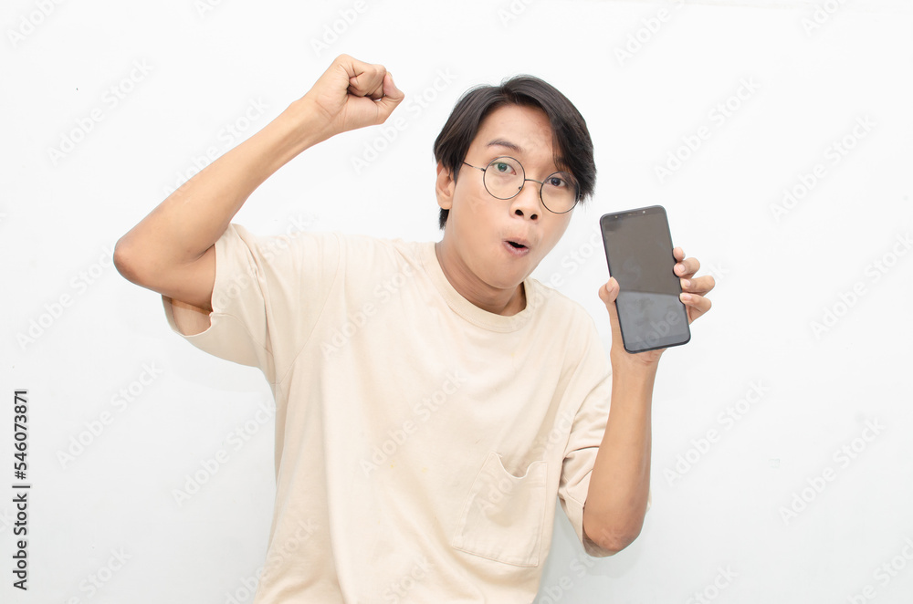 excited young asian man in beige tshirt holding and showing phone screen with happy euphoric shocked wow expression. man pointing to screen phone with thumb up. billboard model advertisment concept. excited young asian man in beige tshirt holding and showing phone screen with happy euphoric shocked wow expression. man pointing to screen phone with thumb up. billboard model advertisment concept.