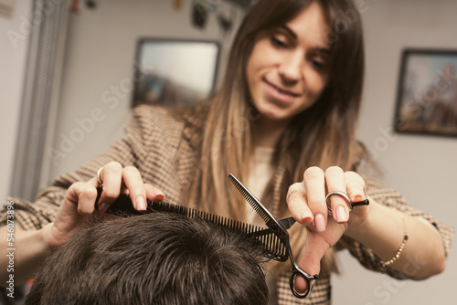 Young man getting a modern haircut. Girl hairdresser cuts a guy with scissors. Men's fashion and style. Hair care, beauty industry, barber concept. Barber shop men hairstyle