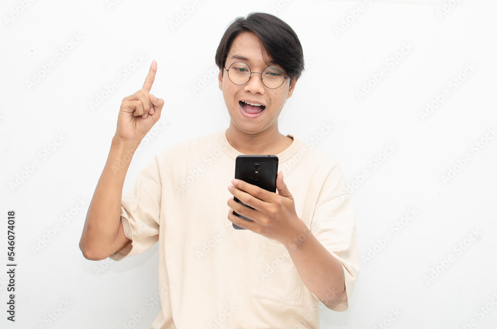 excited young asian man in beige tshirt holding and showing phone screen with happy euphoric shocked wow expression. man pointing to screen phone with thumb up. billboard model advertisment concept. excited young asian man in beige tshirt holding and showing phone screen with happy euphoric shocked wow expression. man pointing to screen phone with thumb up. billboard model advertisment concept.