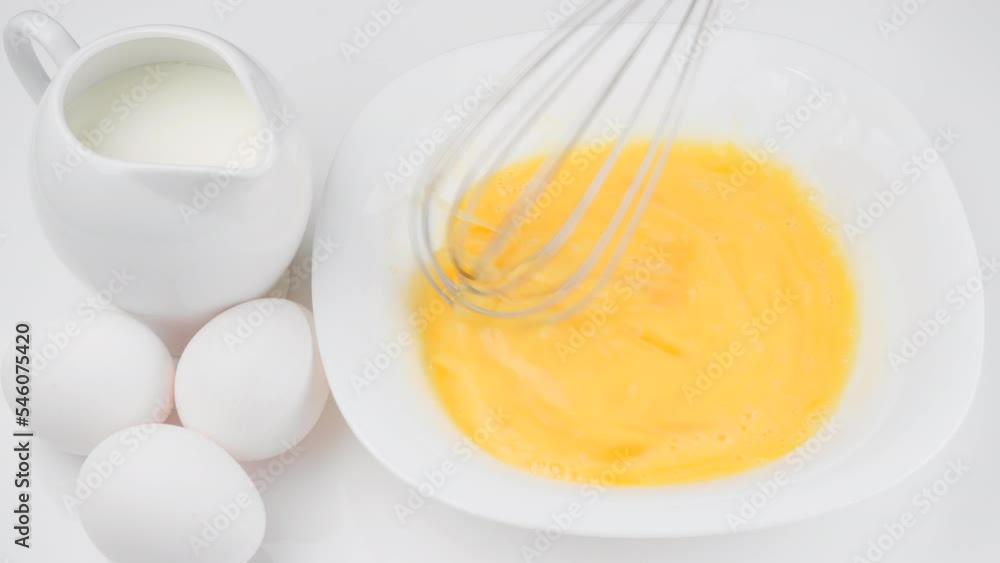 Stirring eggs with whisk . Сhef whisking eggs in white bowl, cooking omelette with milk Stirring eggs with whisk . Сhef whisking eggs in white bowl, cooking omelette with milk