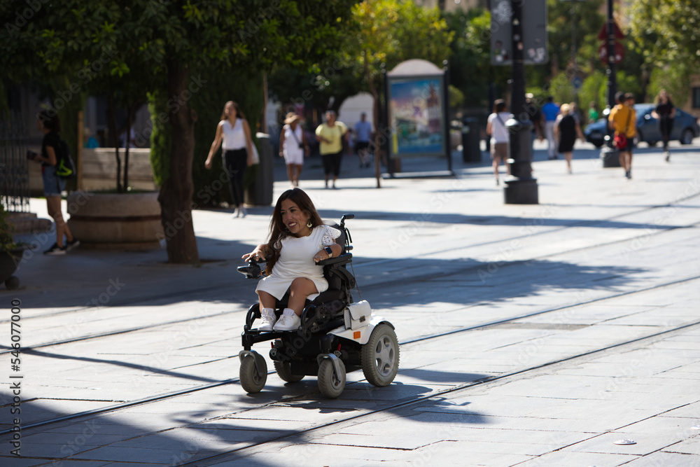 beautiful young disabled woman in wheelchair and reduced mobility enjoys her trip around the city where she is on vacation.