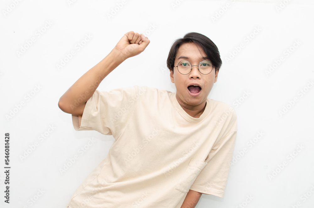 Asian young man wearing casual beige tshirt surprised, amazed, wow shocked raising arms gesturing victory and yes gesture