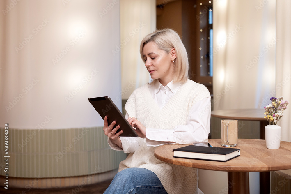 A cute girl is sitting with a tablet and a diary in a cafe and drinking coffee A cute girl is sitting with a tablet and a diary in a cafe and drinking coffee