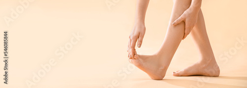 Young woman making foot massage on beige background with space for text