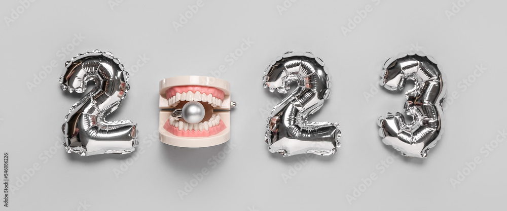 Balloons in shape of figure 2023 and model of jaw with Christmas ball on grey background Balloons in shape of figure 2023 and model of jaw with Christmas ball on grey background