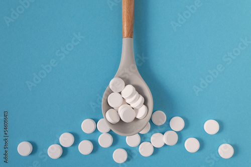 White large vitamin pills in a beautiful spoon on a blue background with place to insert text. Medicine and health.