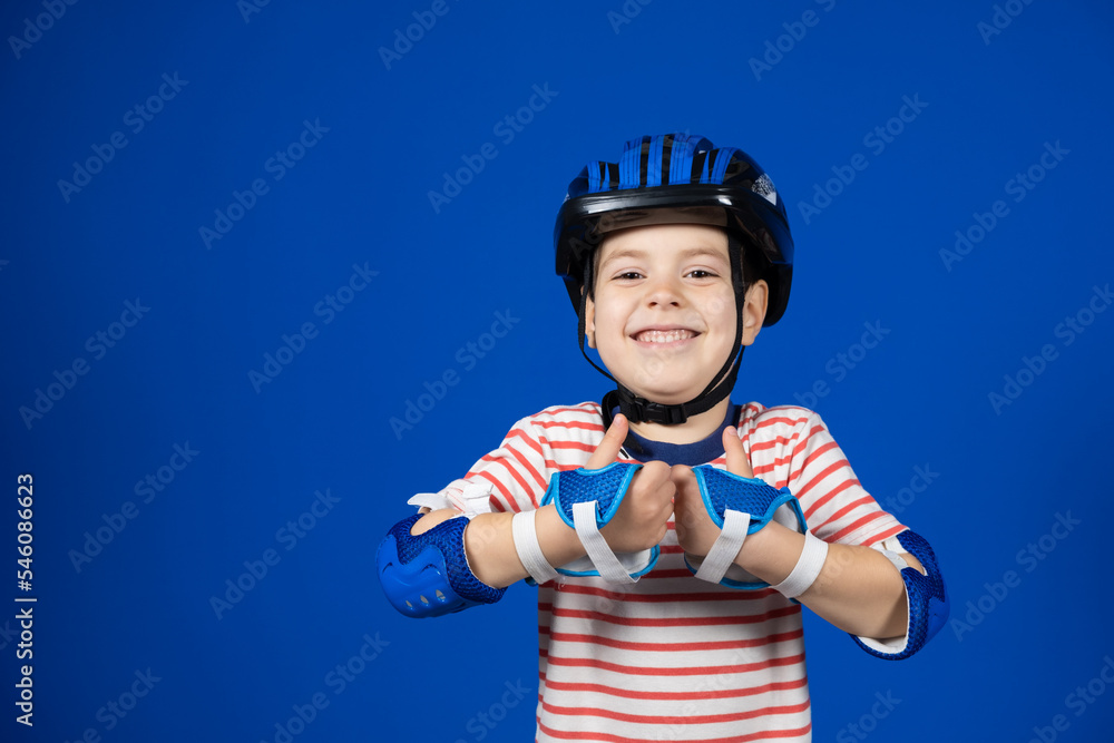 A boy in a helmet and gloves shows thumbs up on a blue background A boy in a helmet and gloves shows thumbs up on a blue background