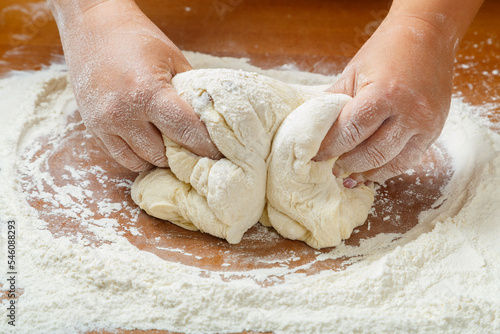 The hands of a Jewish woman knead the dough for wicker challahs for the holiday on the table.