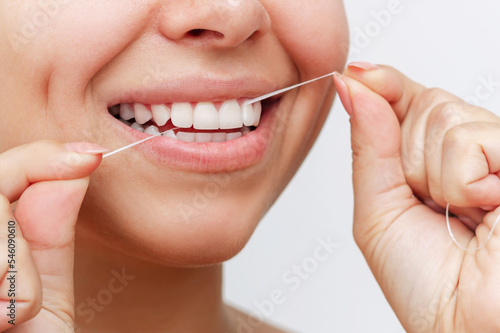 Fotografie Close-up of a young woman flossing her teeth after meal on white background