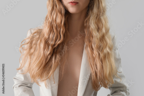 Young blonde woman in stylish jacket on light background