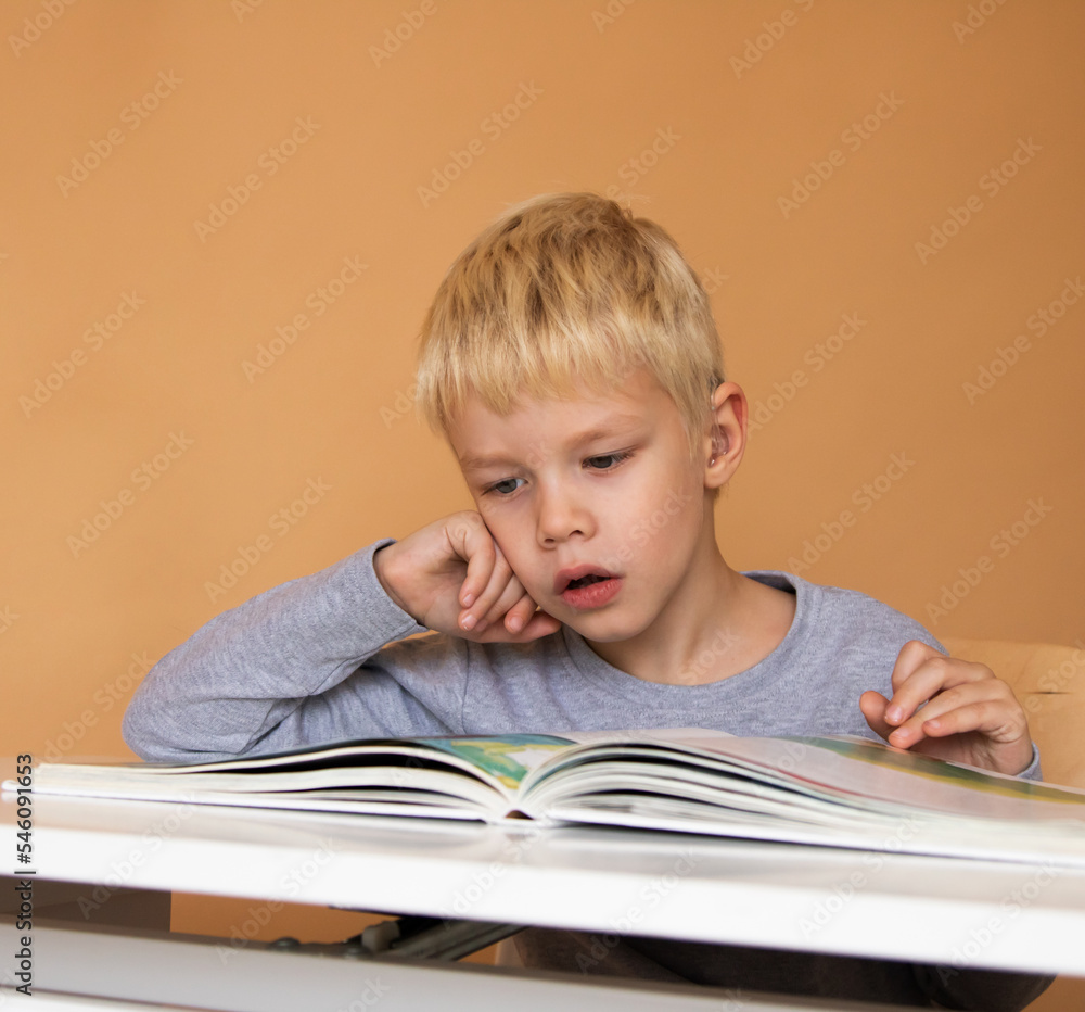 Little boy with hearing aid reading book indoors Little boy with hearing aid reading book indoors