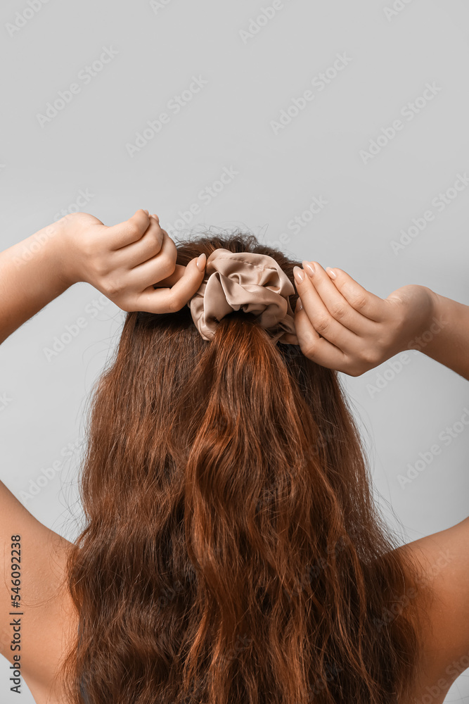 Naklejka premium Woman adjusting silk scrunchy on light background
