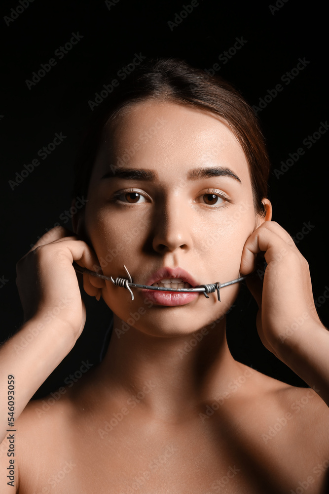 Young woman with barbed wire in mouth on dark background. Censorship concept Young woman with barbed wire in mouth on dark background. Censorship concept