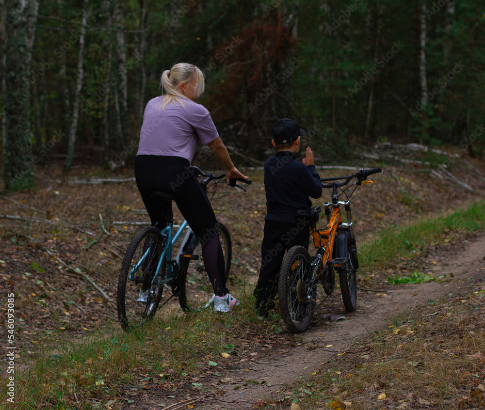 The child explains to his mother where to ride a bicycle along a forest path. Outdoor weekends. Traveling mother and son on a bicycle through the forest. The concept of a healthy lifestyle.