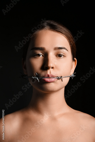 Young woman with barbed wire in mouth on dark background. Censorship concept